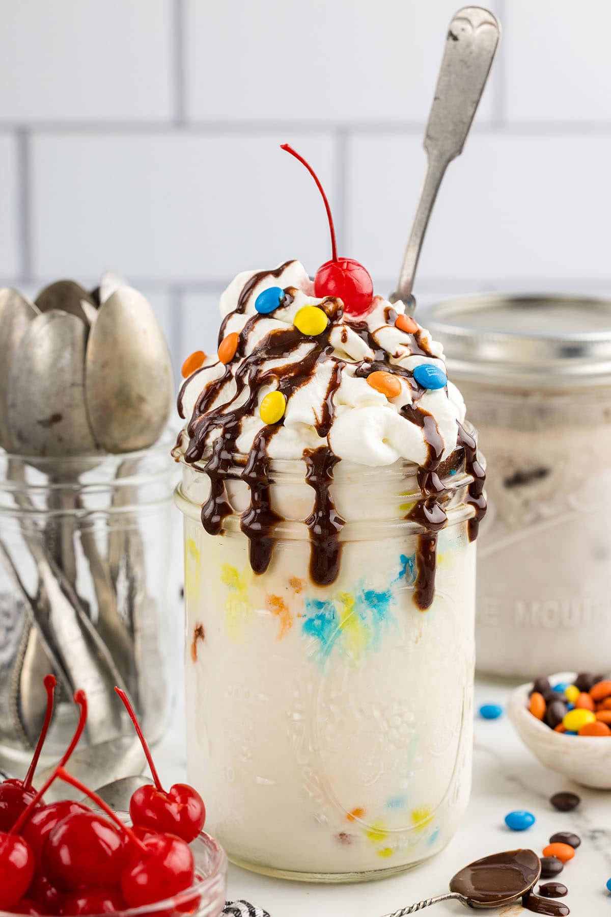 Mason Jar Ice Cream topped with M&M's, chocolate syrup and cherry.