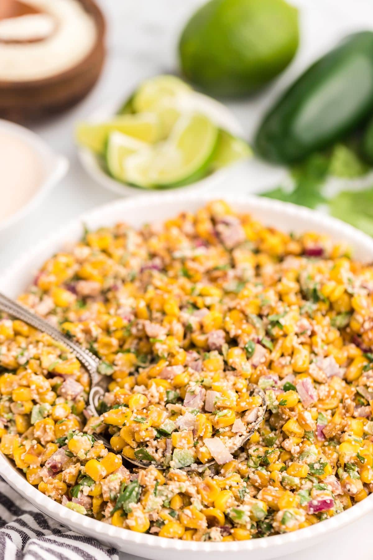 mexican corn salad in a white plate with a spoon.