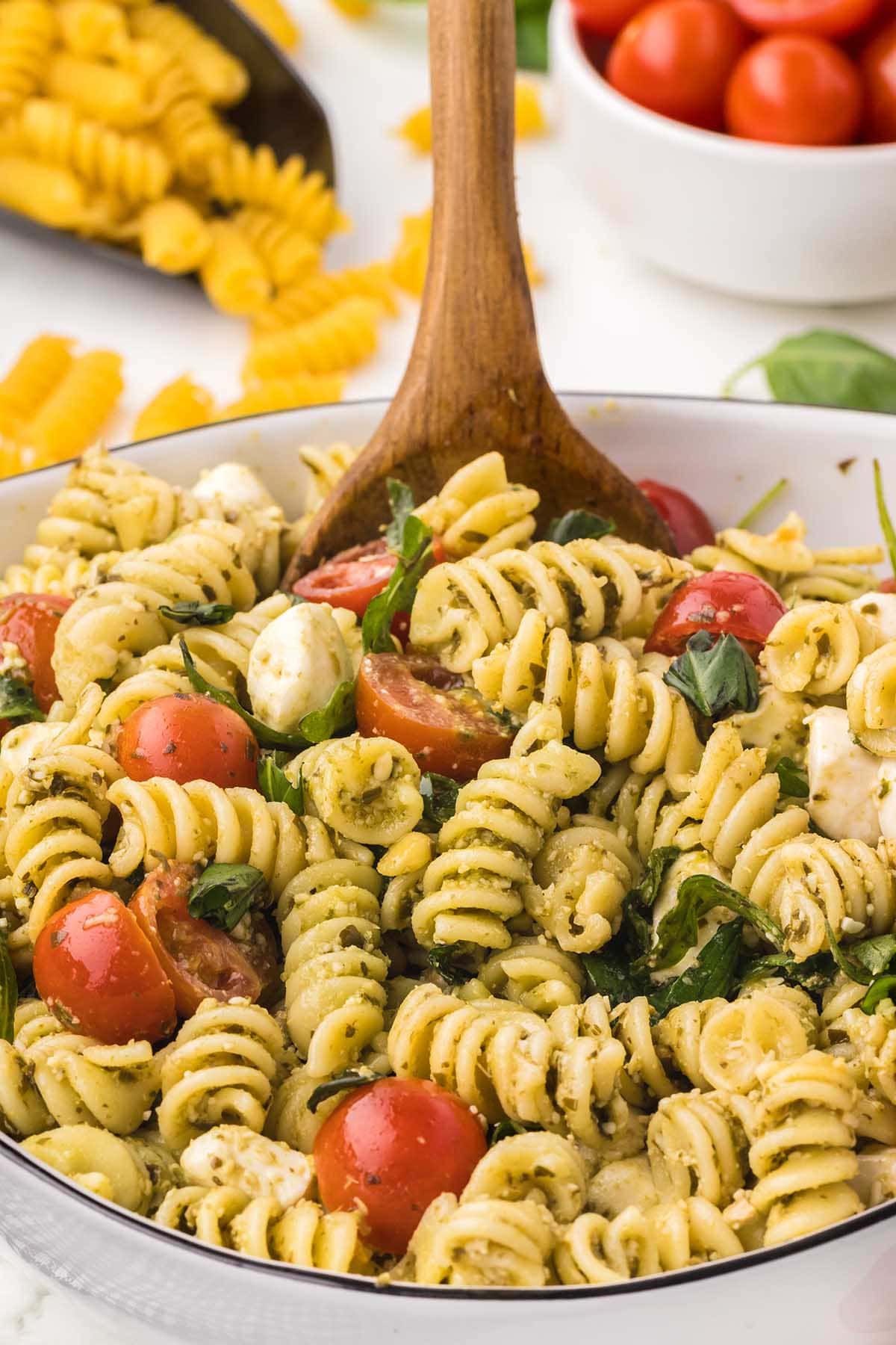 a large bowl of Pesto Pasta Salad and extra tomatoes at the back.