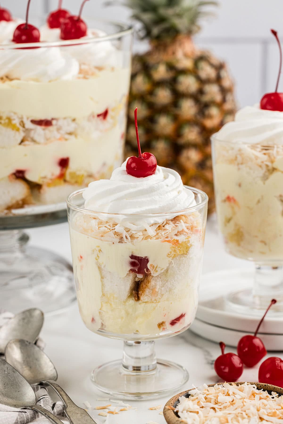 Pina Colada Trifle served in a dessert glass topped with cool whip and a cherry.