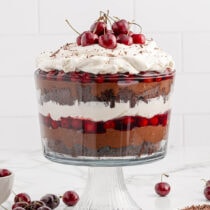 Black Forest Trifle in a trifle container topped with cool whip and cherries.