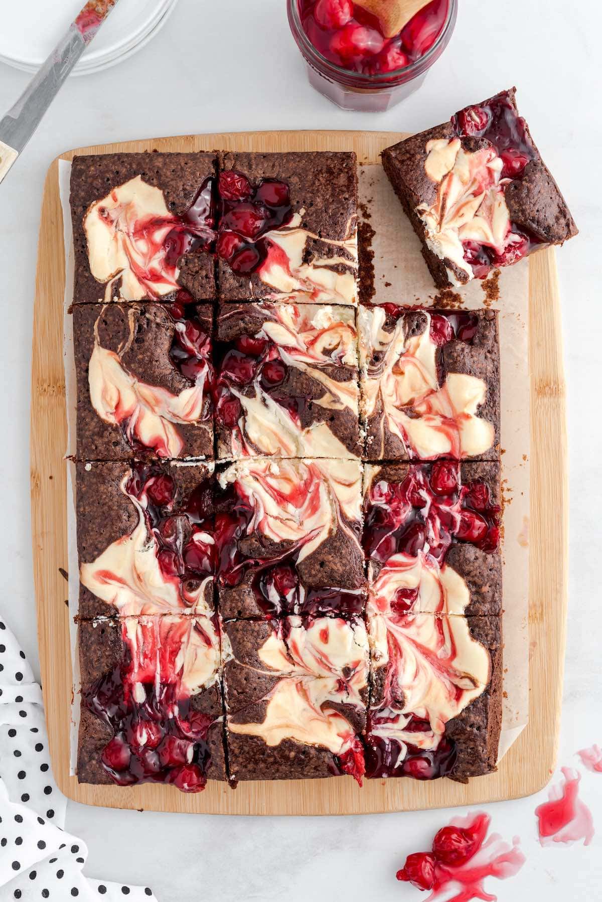 Cherry Cheesecake Brownies cut into squares on top of wooden board. 