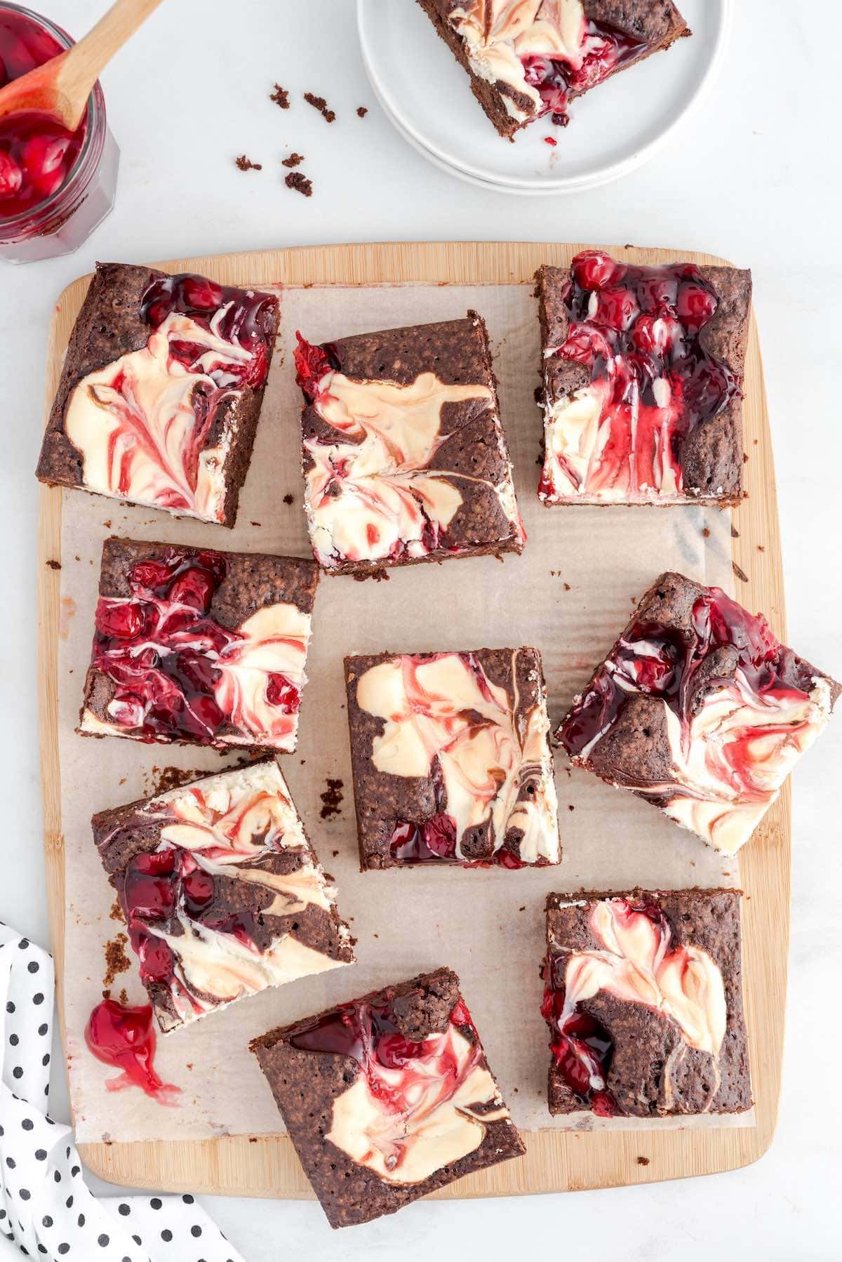 a couple squares of Cherry Cheesecake Brownies scattered on top of a wooden board.