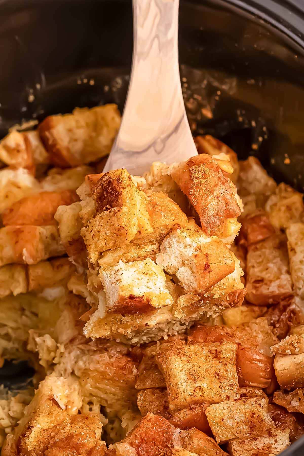 scooped Crockpot French Toast Casserole using a wooden spoon.
