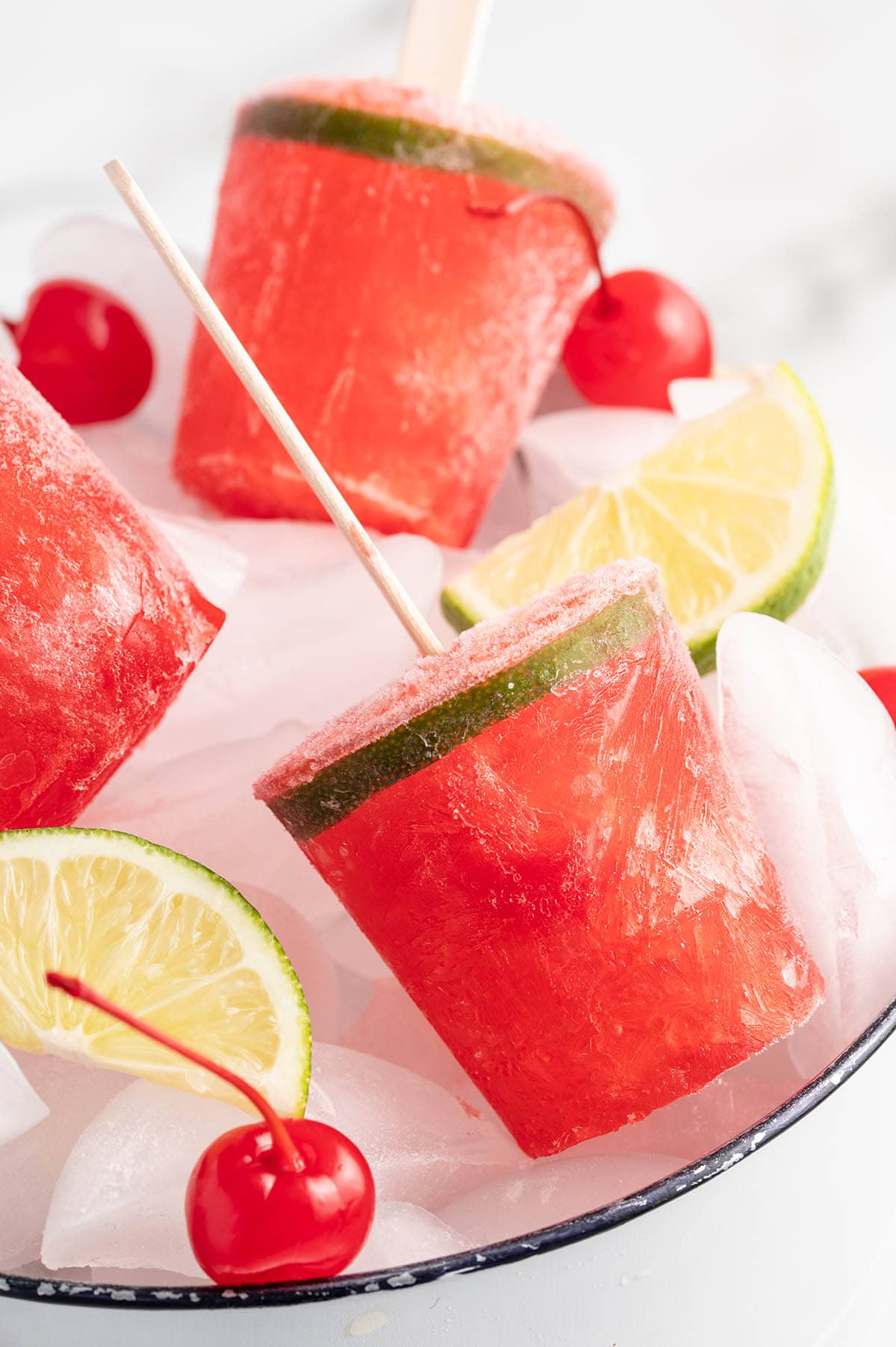 Dirty Shirley Popsicle with cherries and lime inside a plate full of ice cubes.