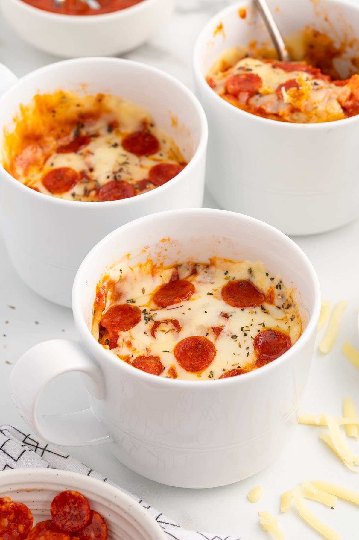 2 glasses of Pizza in a Mug topped with cheese and pepperoni.