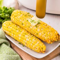 Air Fryer Corn on the Cob placed on a white plate garnished with chopped herbs and melted butter.