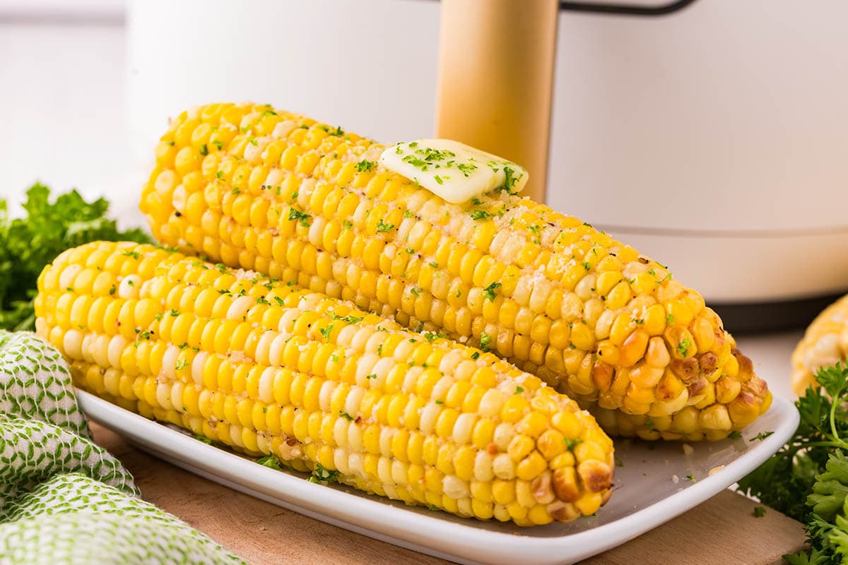 3 corns on a white plate garnished with chopped herbs and melted butter on top.