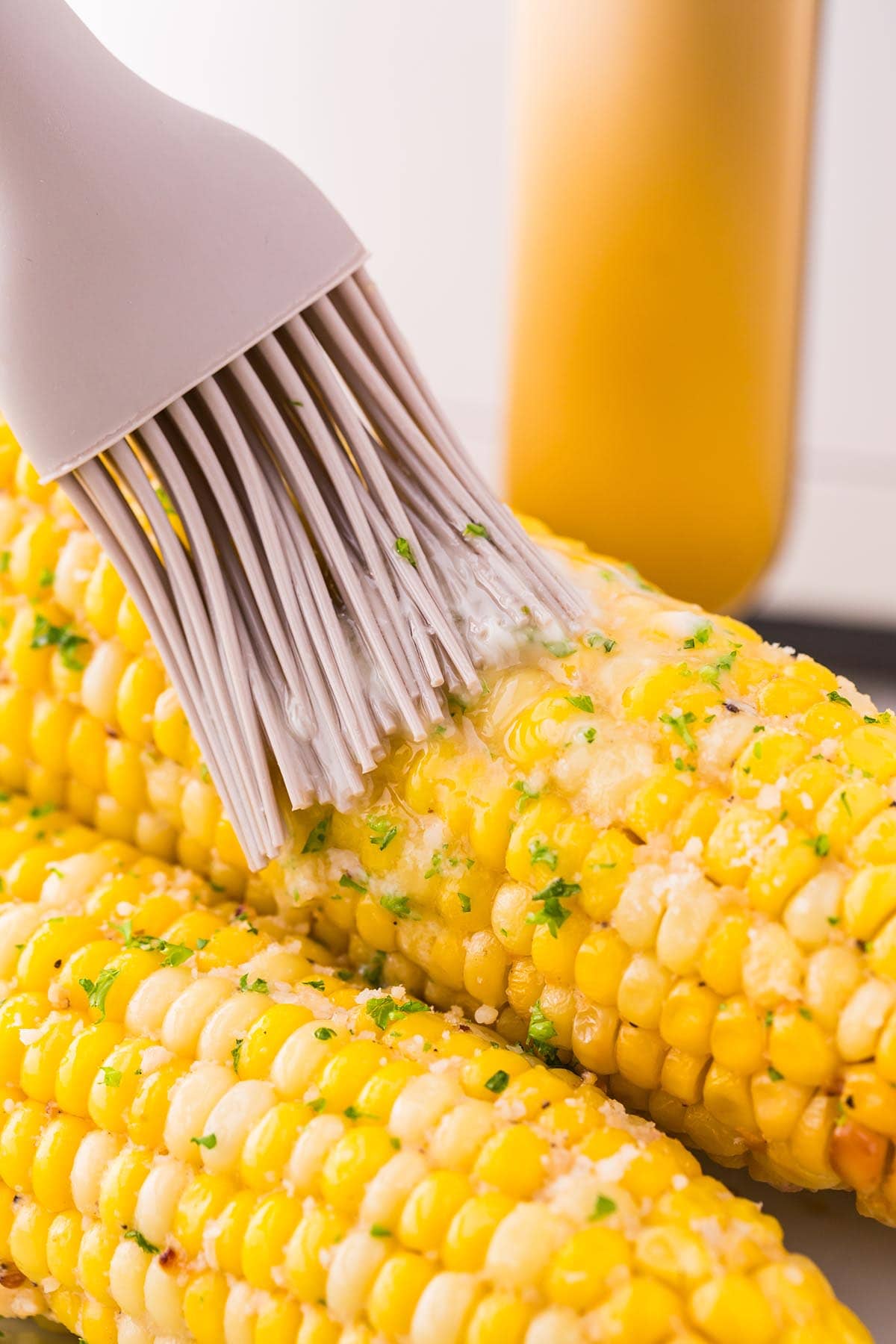 Air Fryer Corn on the Cob brushed with butter using a silicone brush.