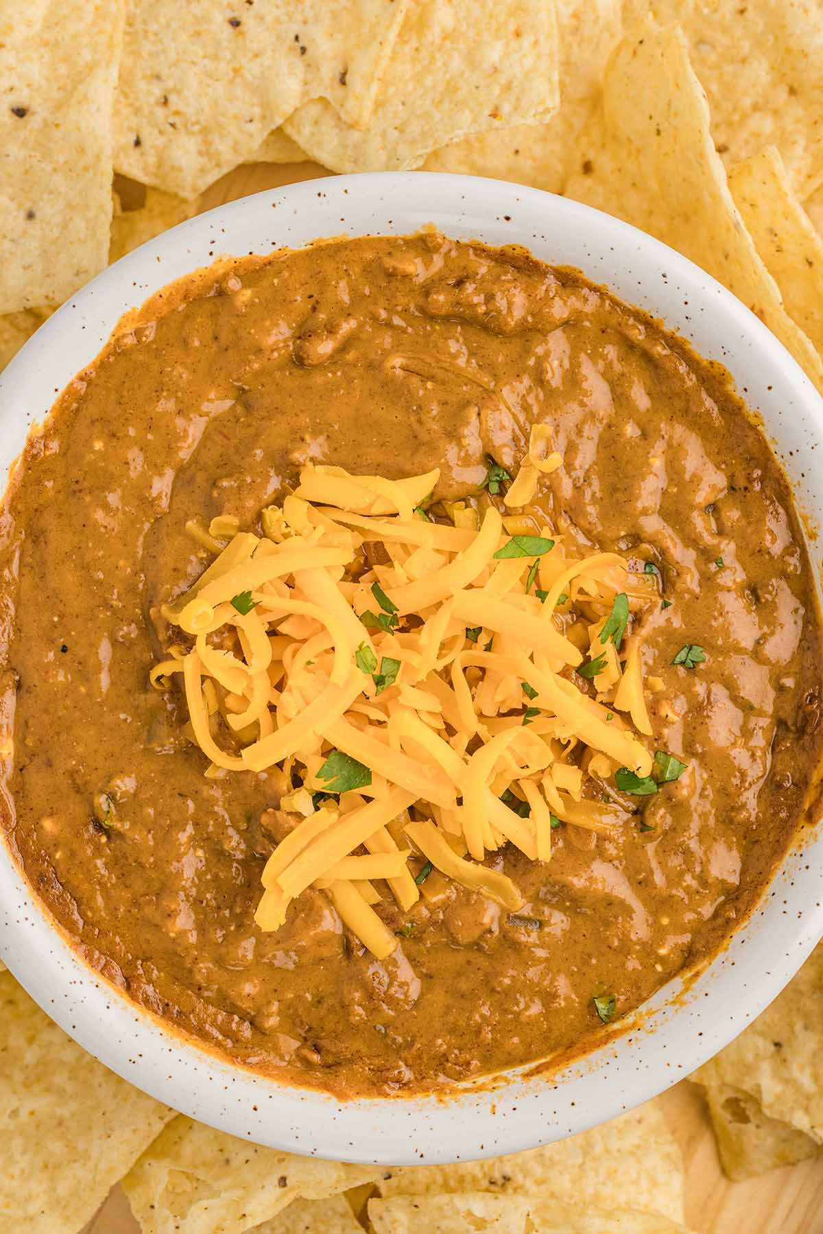 a bowl of chili cheese dip topped with shredded cheese. 