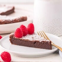 a slice of Flourless Chocolate Torte dusted with powdered sugar and topped with raspberries.