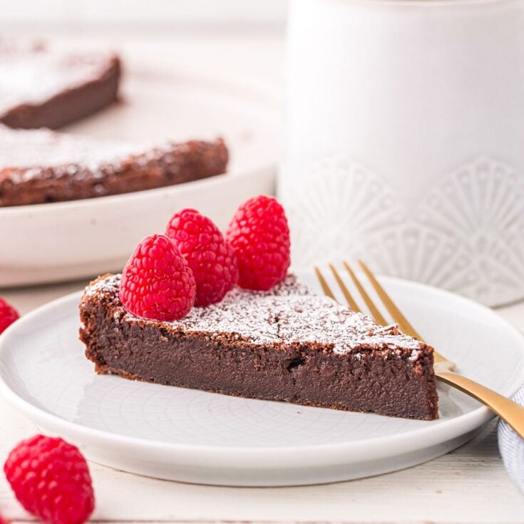 a slice of Flourless Chocolate Torte dusted with powdered sugar and topped with raspberries.