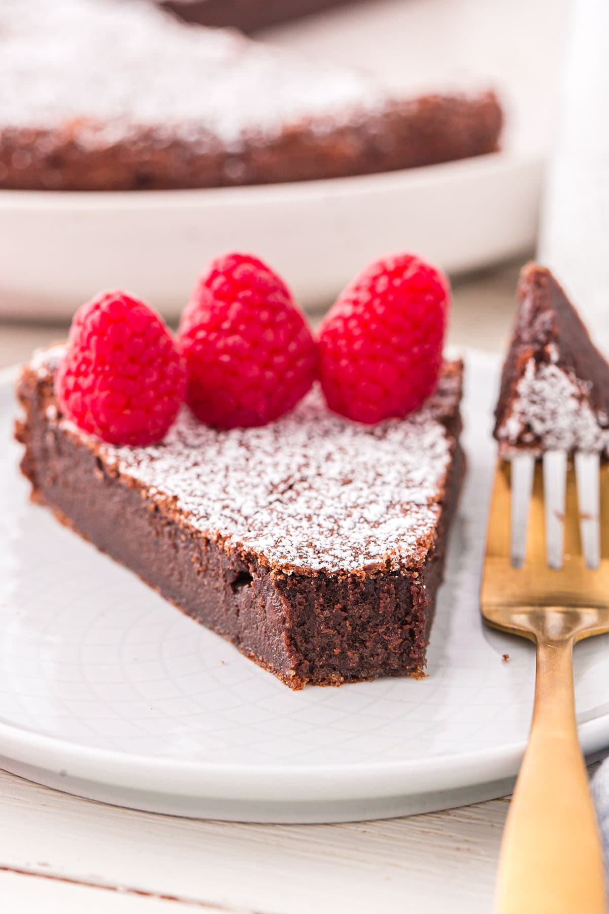 a slice of Flourless Chocolate Torte on a white plate with raspberries on top.