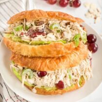 A sandwich on a white plate filled with chicken salad and a few grapes beside it.