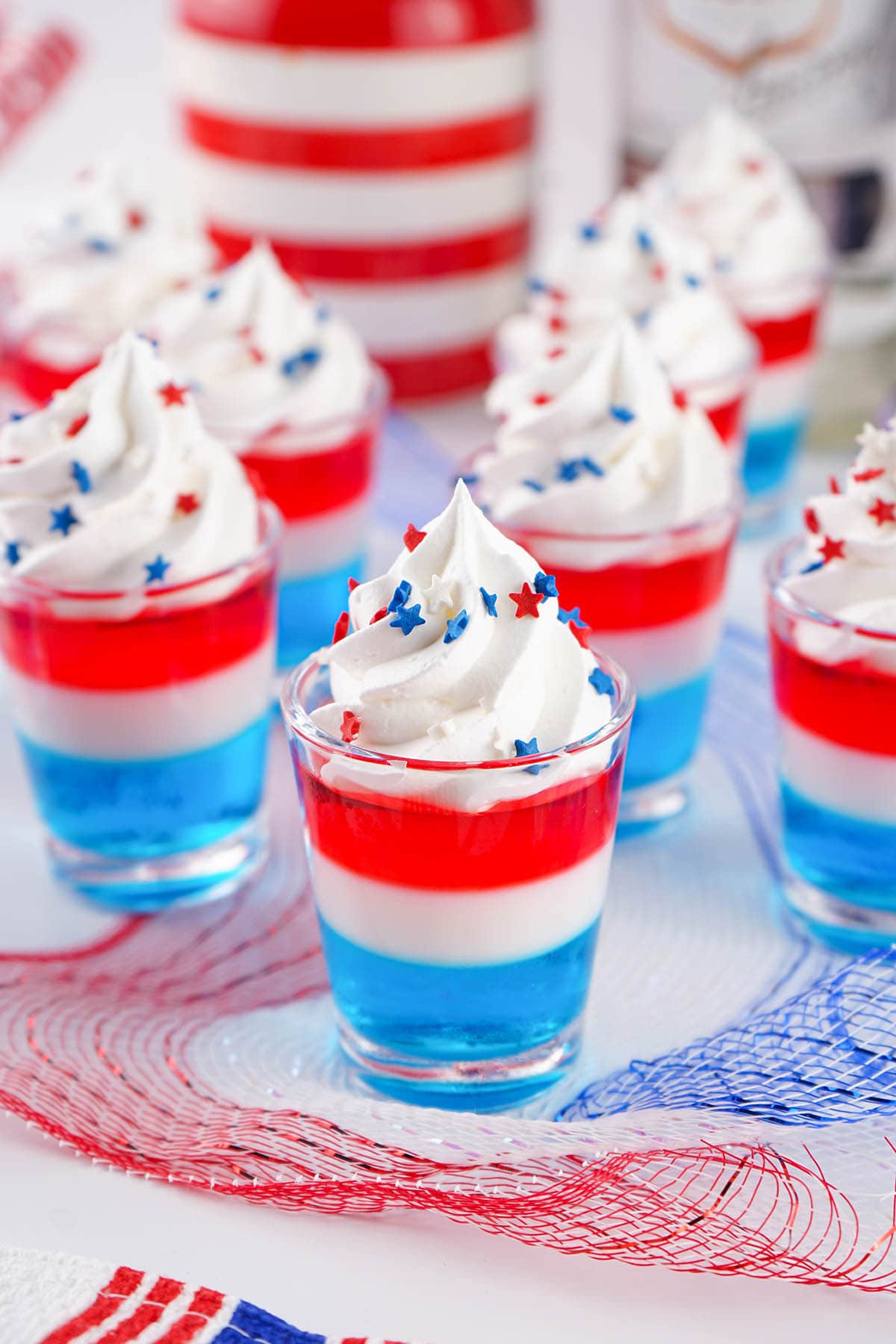 glasses of Red White Blue Jello Shots topped with whipped cream and sprinkles.