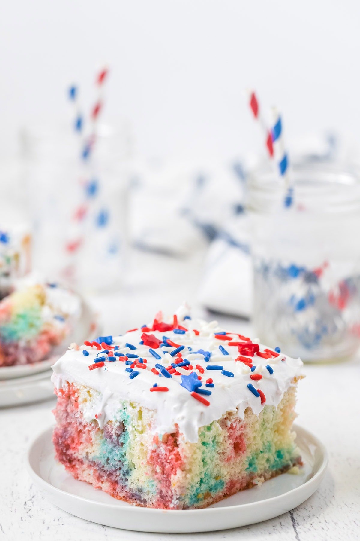 a slice of red white blue poke cake with sprinkles on top. 