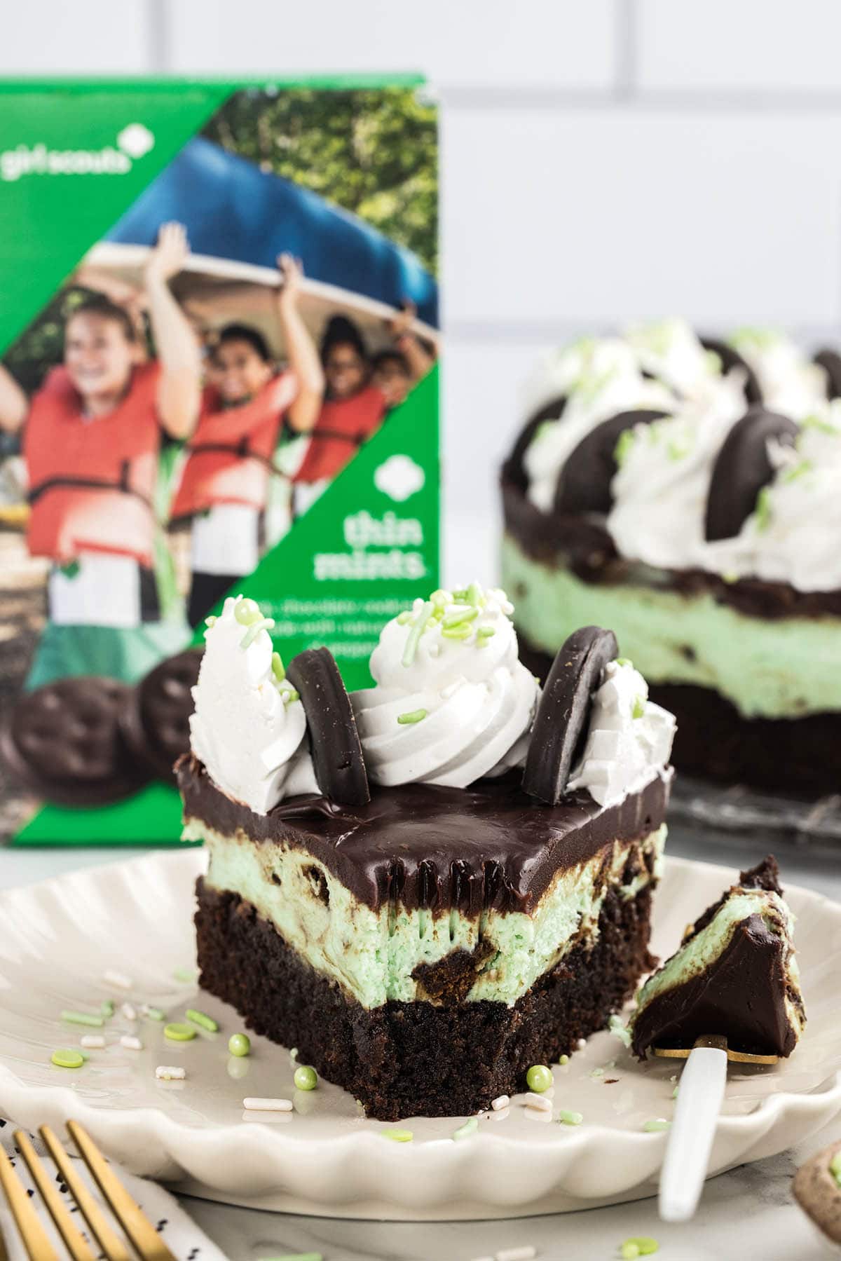 a slice of Thin Mint Cheesecake on a white plate with a box of Thin Mint on the background. 