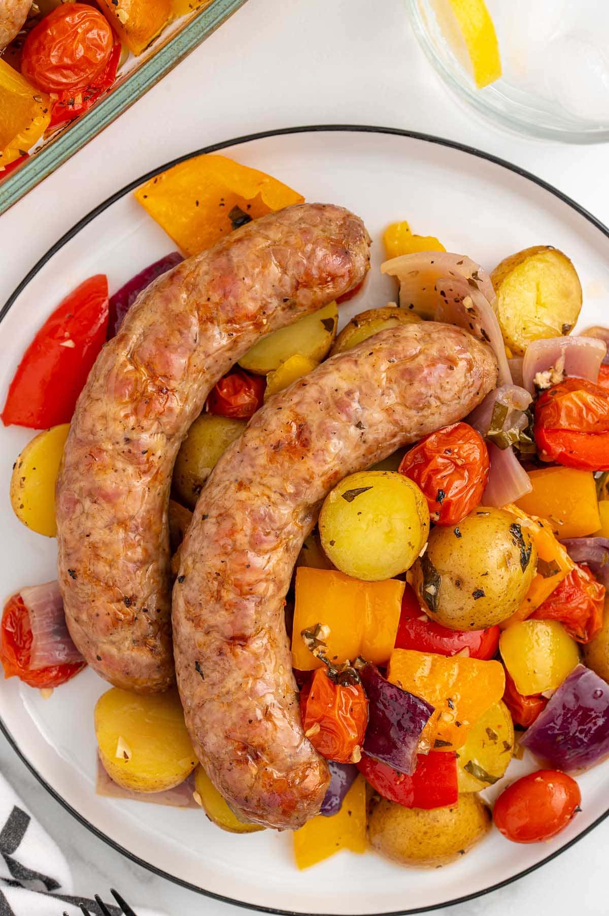 Baked Italian Sausage and vegetables on a white plate.