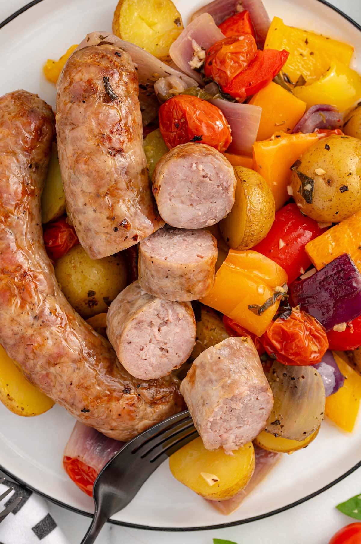 Baked Italian Sausage cut into pieces with vegetables on the plate.