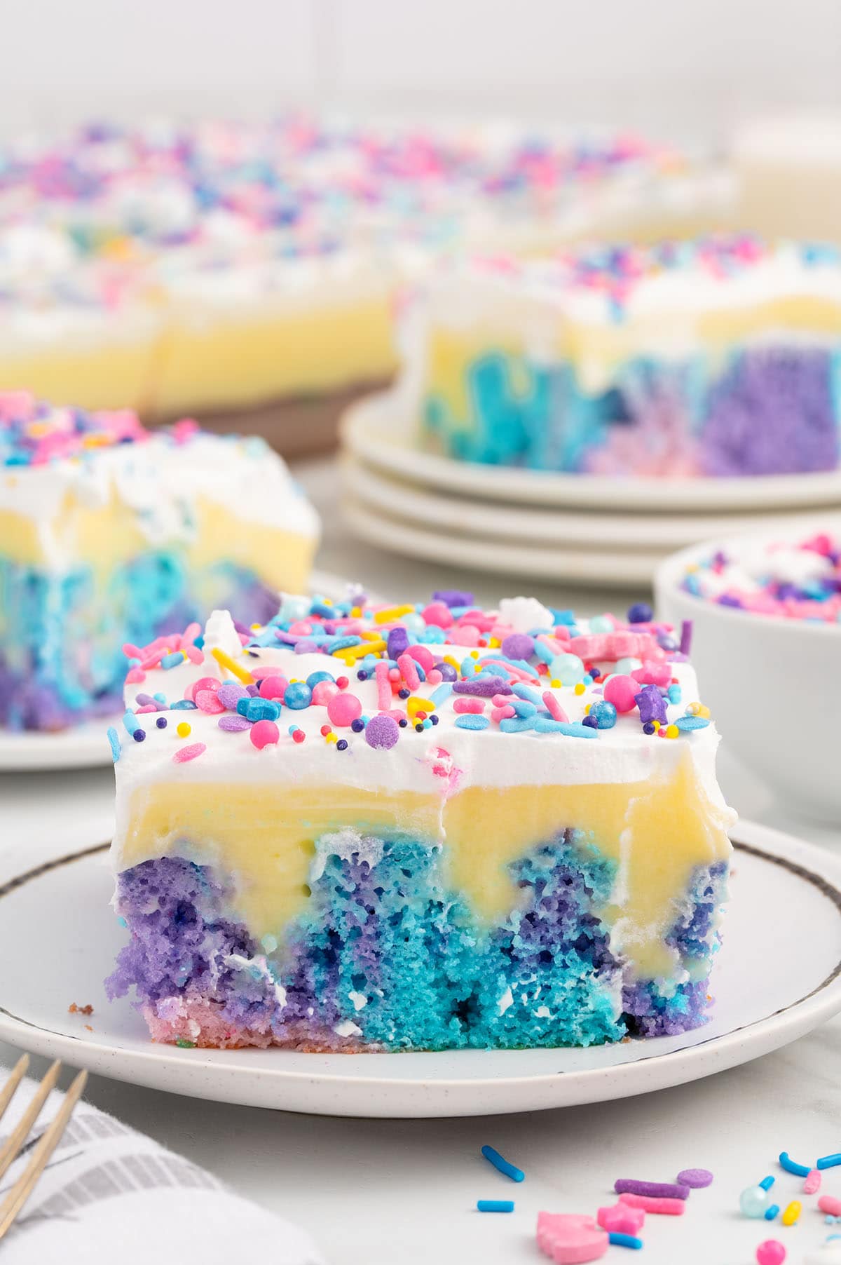 a slice of Unicorn Poke Cake on the plate with sprinkles.