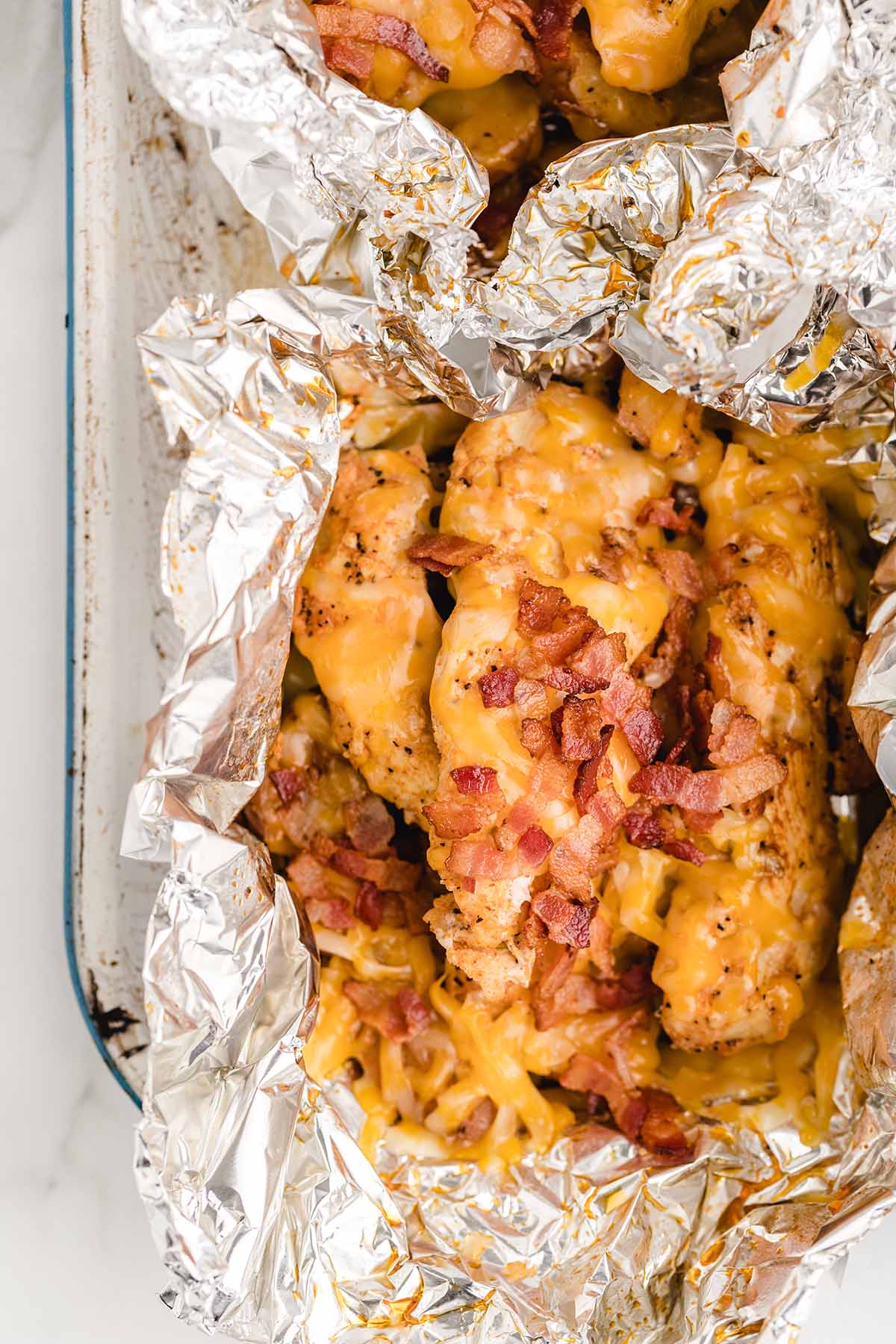 chicken foil packets with cheese and bacon placed on top of baking tray. 