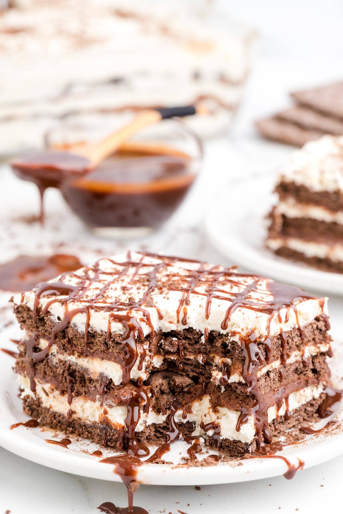 a bitten slice of chocolate icebox cake on a plate drizzled with chocolate syrup. 