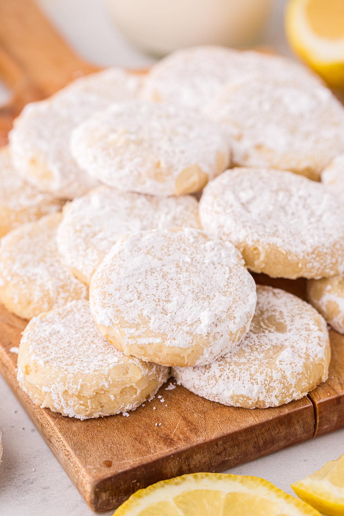 a couple of powdered sugar-covered Lemon Cooler Cookies on a wooden cutting board.