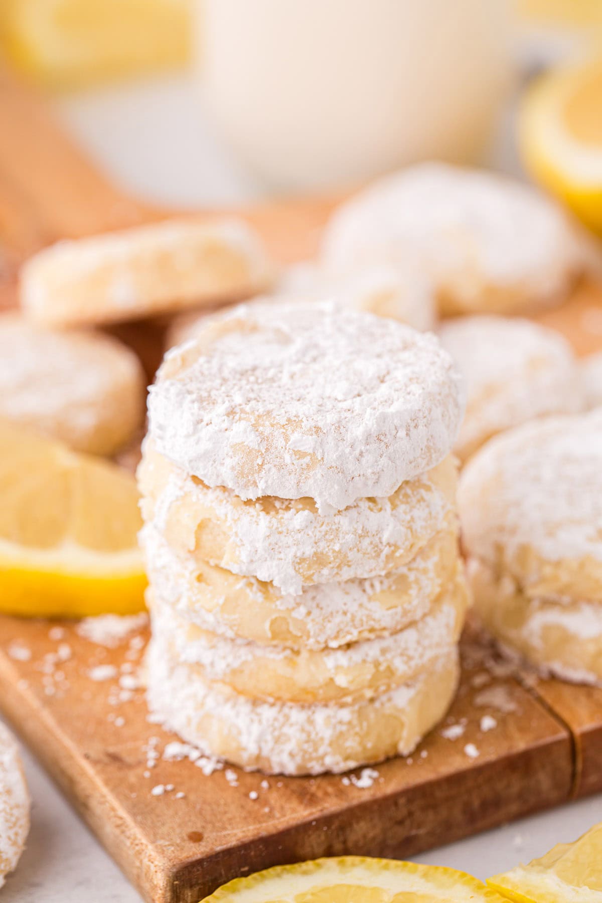 a stack of Lemon Cooler Cookies on a wooden board with slices of lemon in the background.