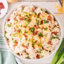Loaded Baked Potato Salad in a large bowl garnished with crumbled bacon, shredded cheese and chopped green onions.