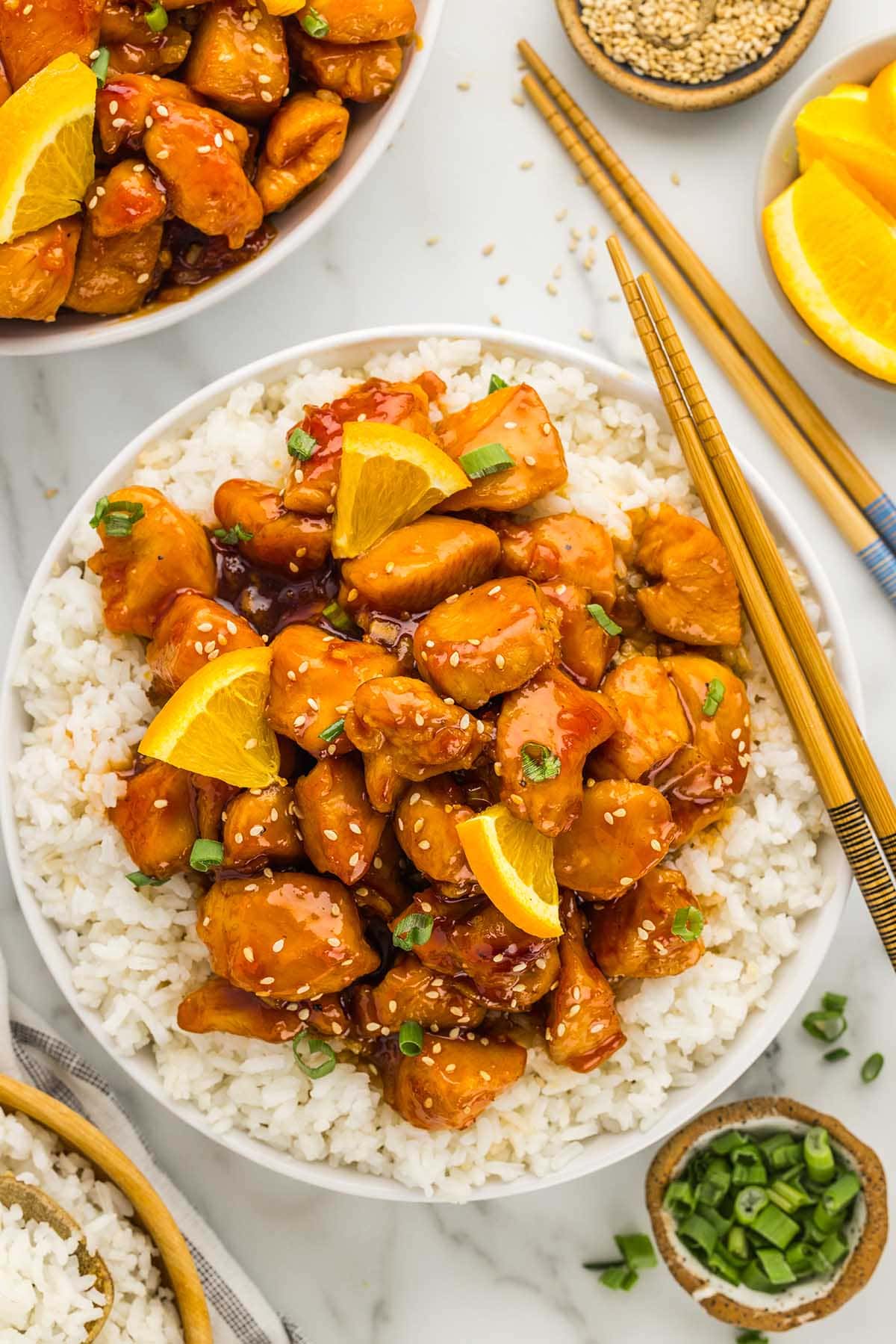 eating orange chicken over a bowl of rice.