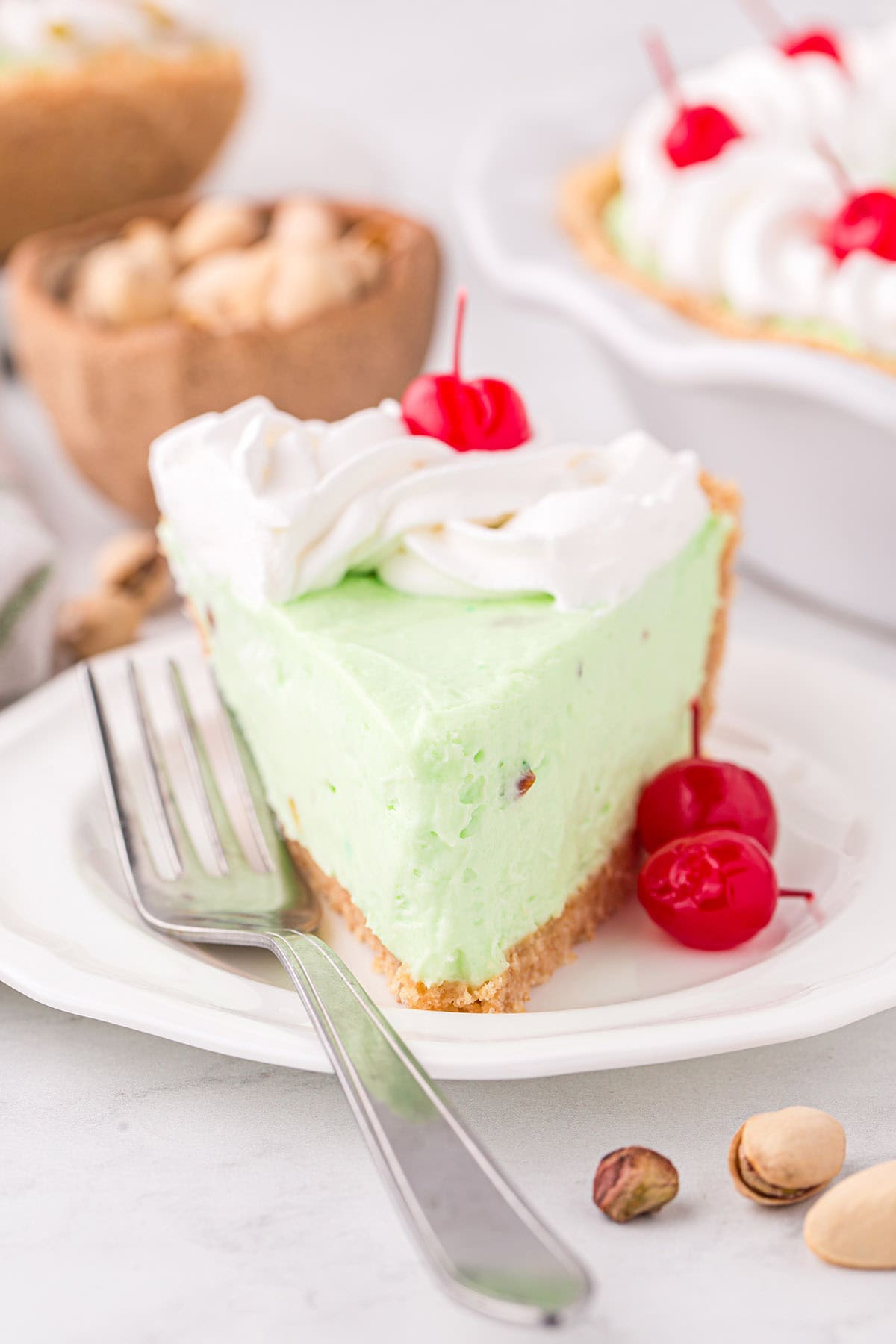 a slice of Pistachio Pie topped with whipped cream and maraschino cherry served on a white plate.