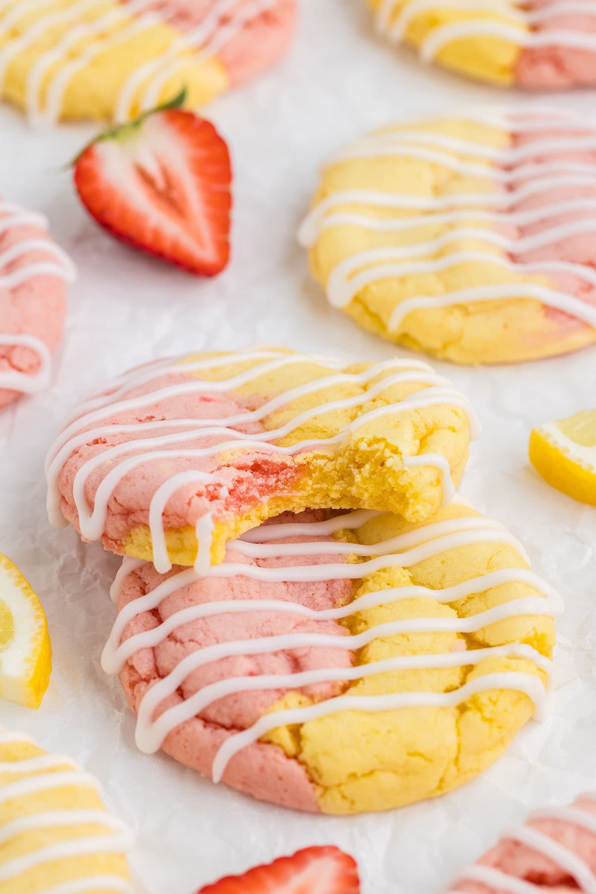 a couple of Strawberry Lemonade Cake Mix Cookies on a white surface drizzled with white icing.