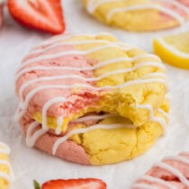 a close up image of Strawberry Lemonade Cake Mix Cookies drizzled with white icing and one cookie has a bite taken out of it.