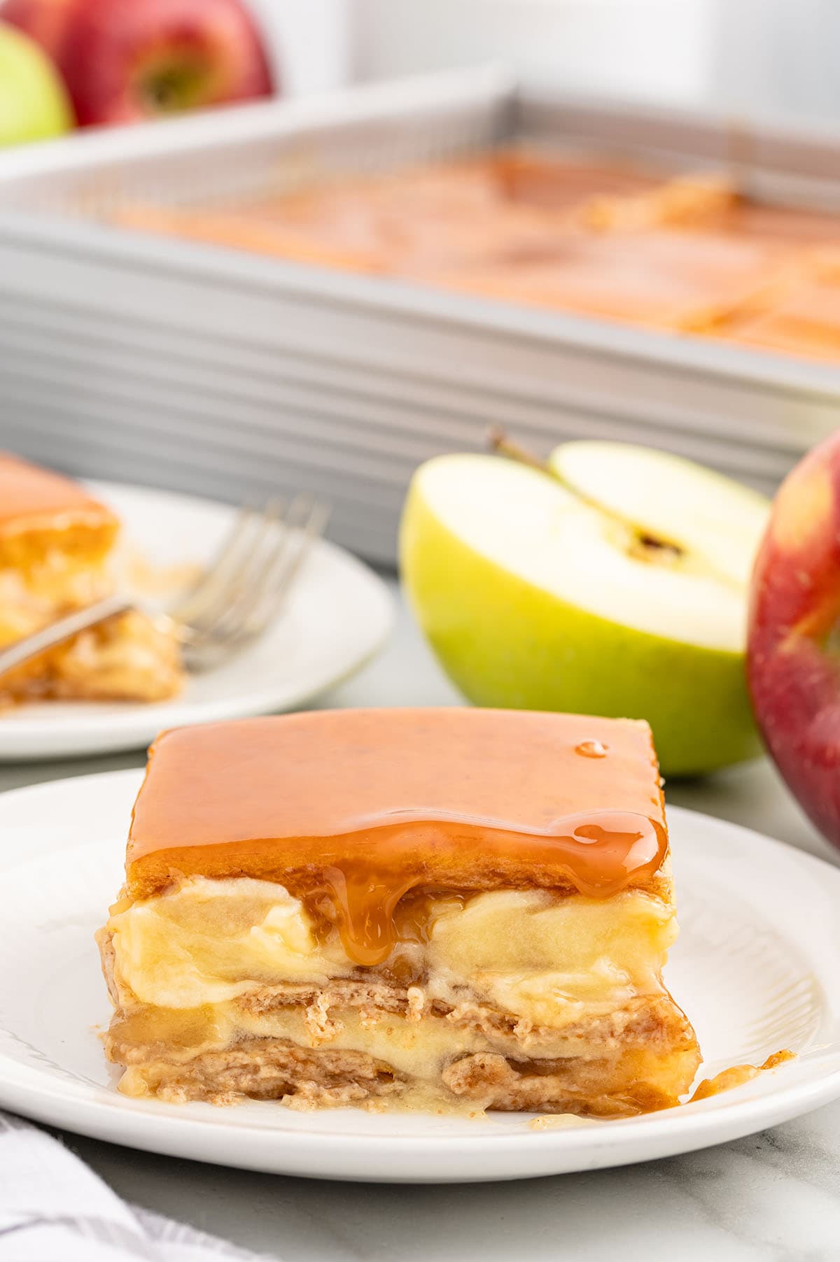 a slice of Caramel Apple Eclair Cake on a white plate with caramel sundae on top.