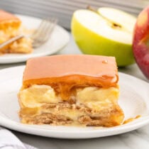 a slice of Caramel Apple Eclair Cake on a white plate and a halved apple in the background.