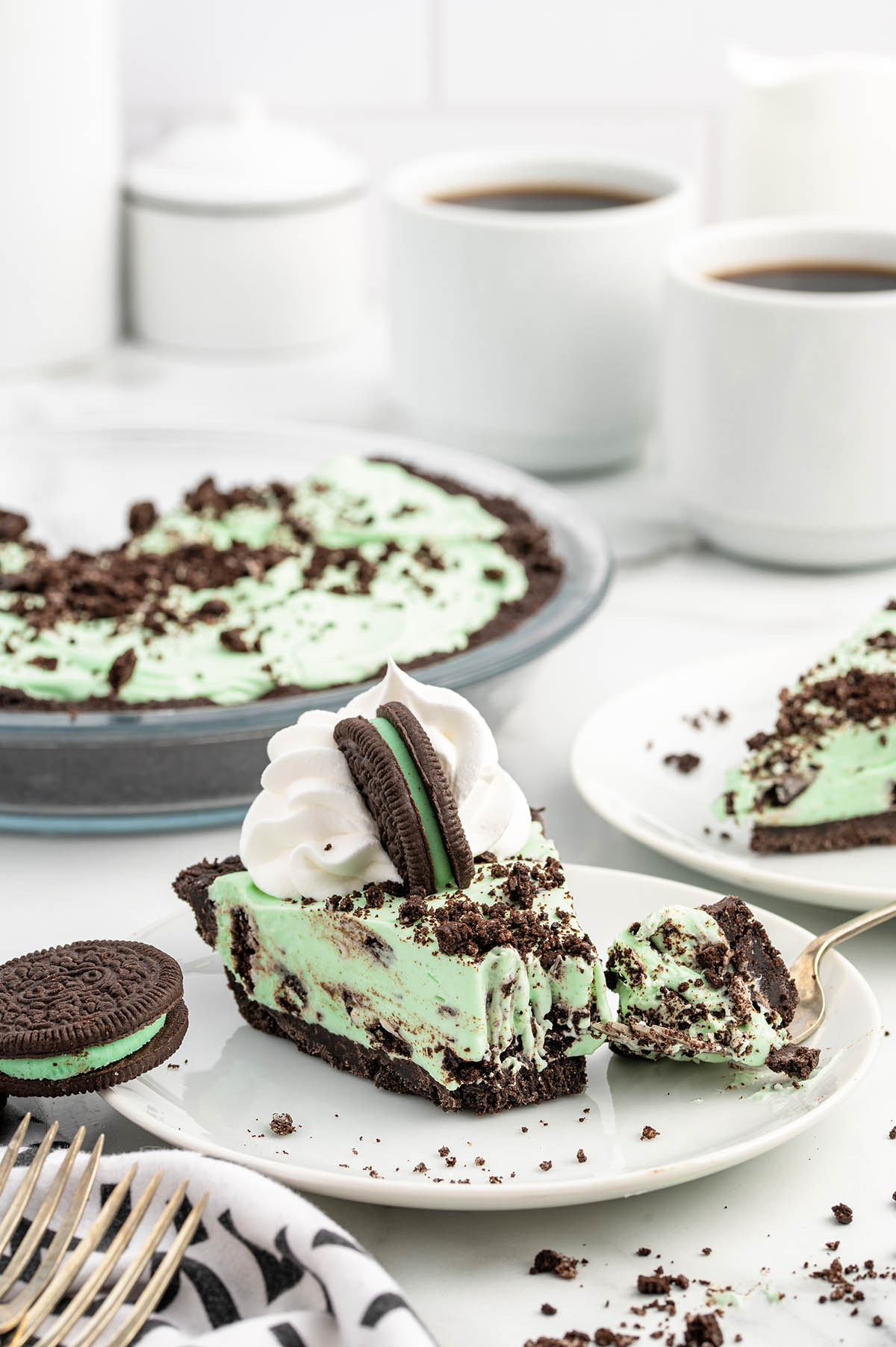 a slice of Mint Chocolate Pie on a white plate with whipped cream and sandwich cookie on top.