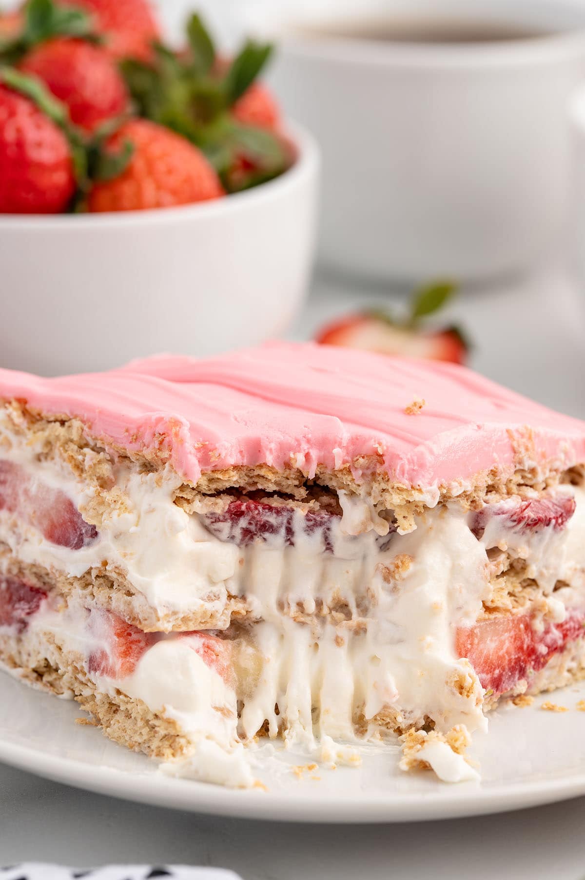 a slice of a layered Strawberry Eclair Cake on a white plate with strawberry frosting on top.