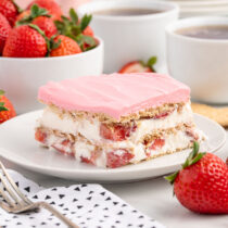 a slice of Strawberry Eclair Cake on a white plate with fresh strawberries on the background.