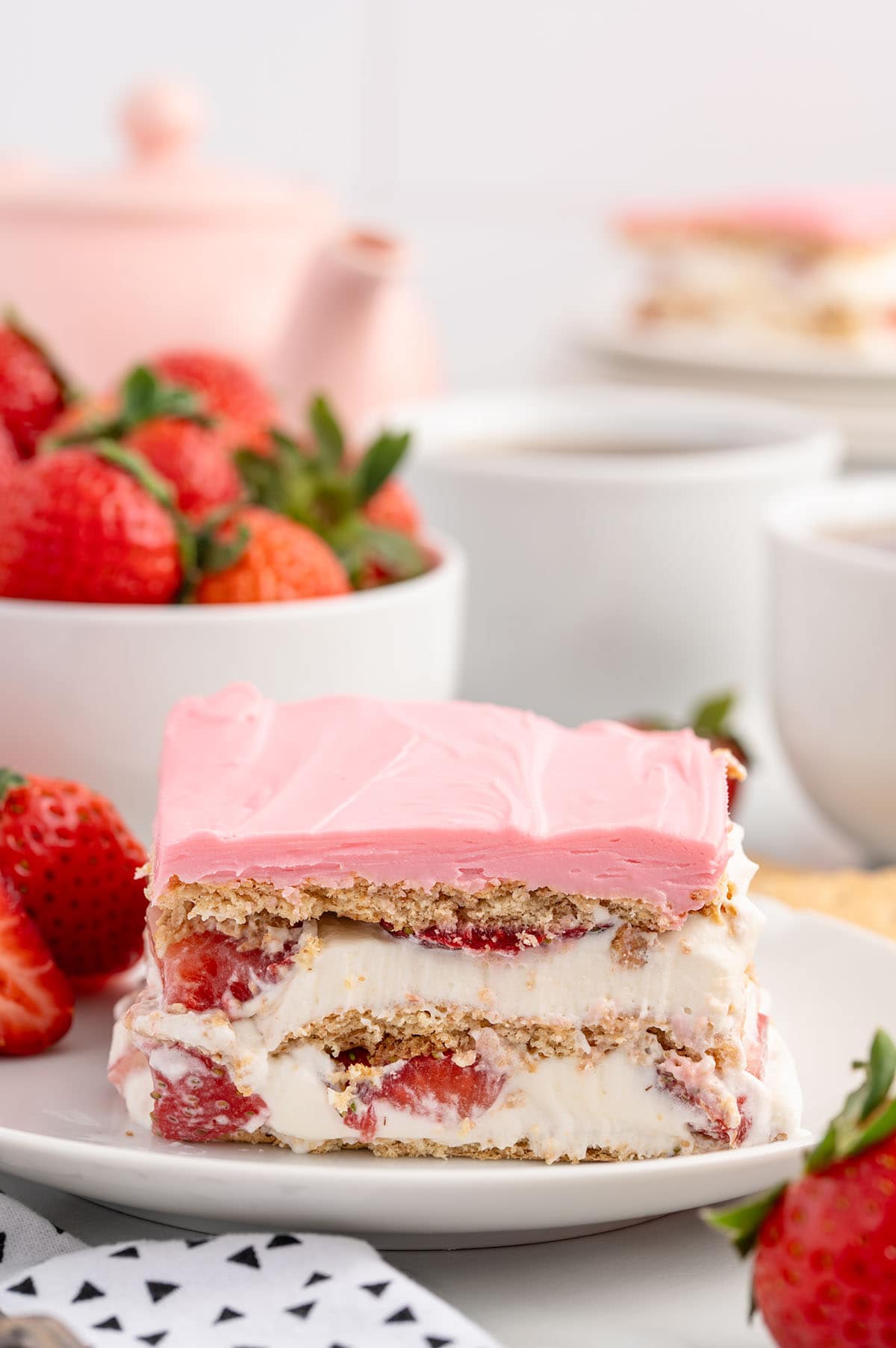 a slice of Strawberry Eclair Cake on a white plate topped with pink layer of frosting.