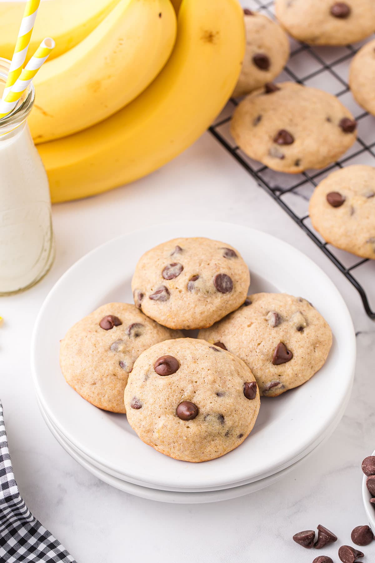 a plate of Banana Bread Cookies with chocolate chips and a bunch of banana in the background.