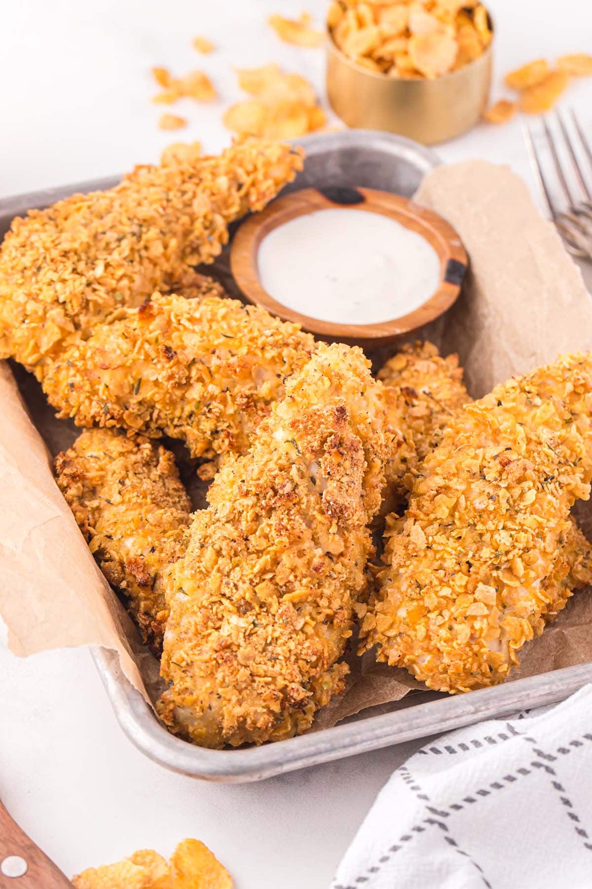 a couple of Cornflake Chicken in a tray served with a bowl of dipping sauce.