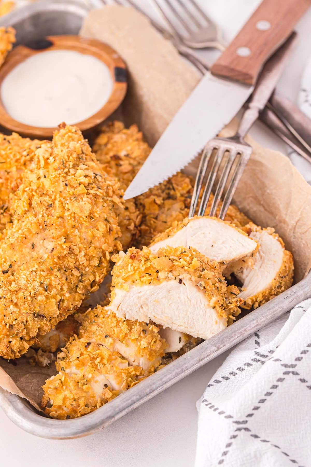 a slices of Cornflake Chicken in a tray with fork and knife.