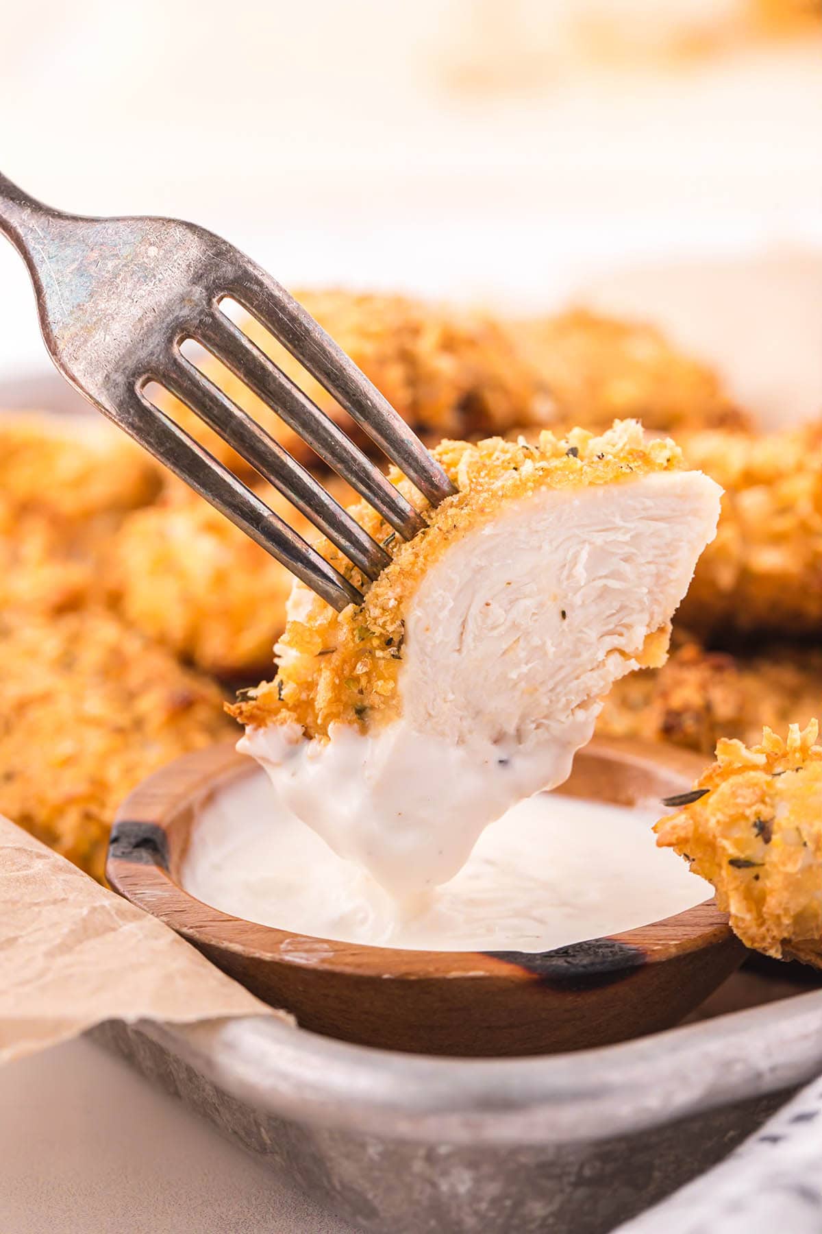 a fork holding a piece of Cornflake Chicken being dipped into a small bowl of creamy sauce.