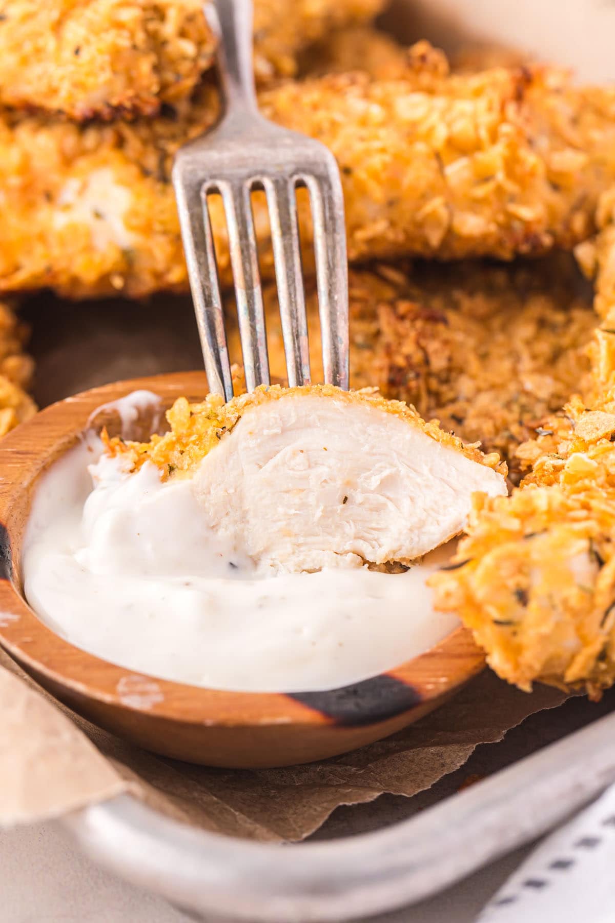 a fork holds a piece of Cornflake Chicken dipped in creamy sauce.