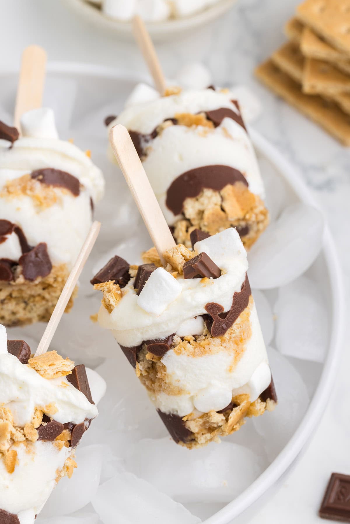 a couple of Layered S'mores Pops over an ice bucket.