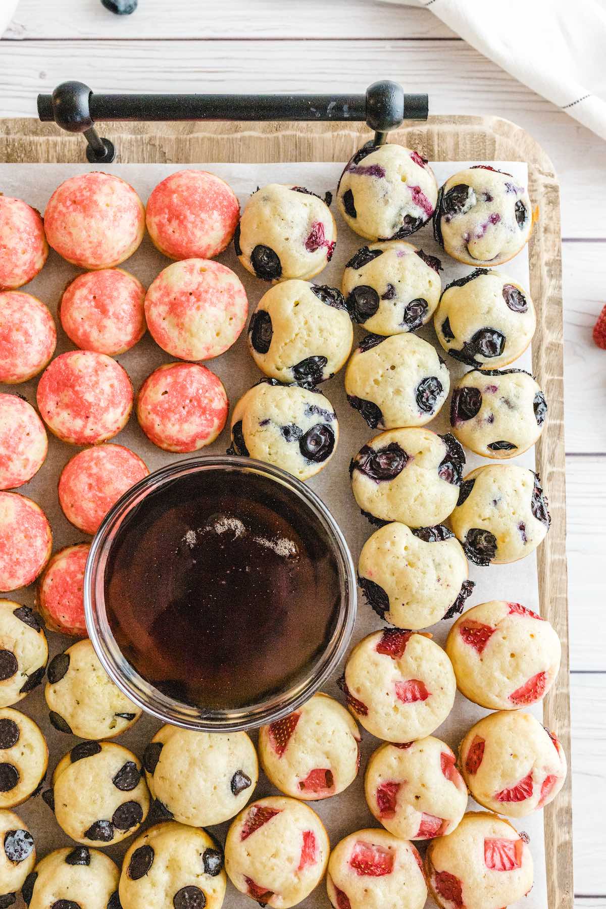 a couple of mini pancake bites on top of wooden tray with syrup in the middle. 