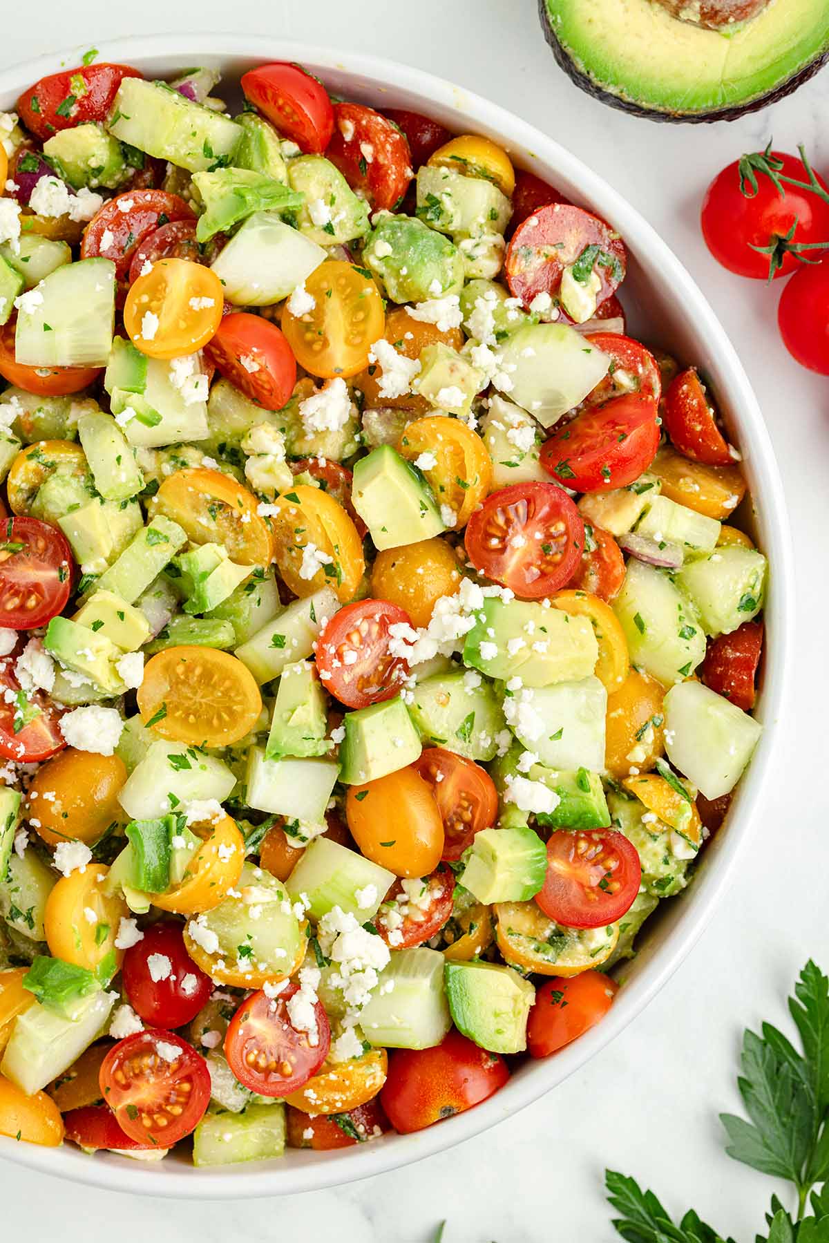 a bowl of Tomato Cucumber Avocado Salad garnished with fresh herbs.