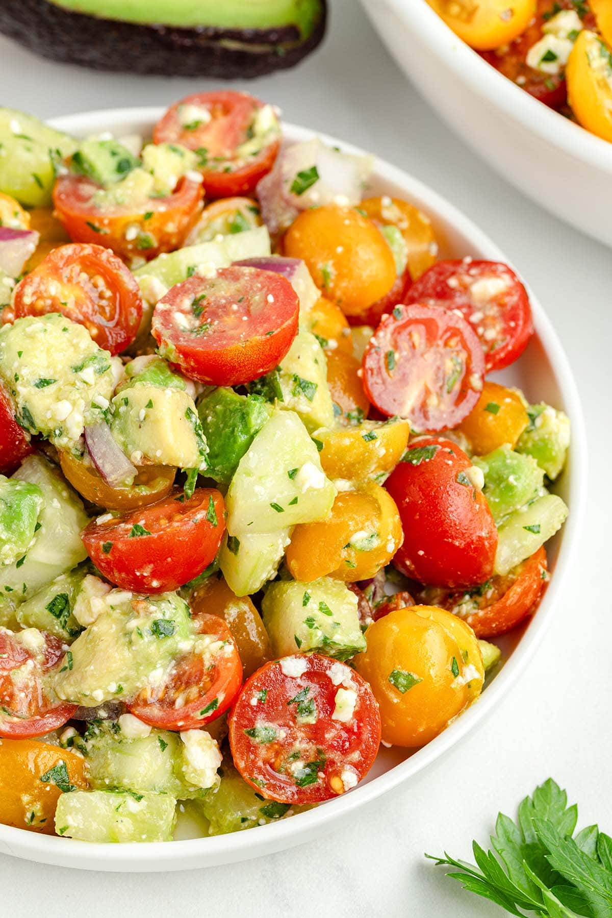 a bowl of Tomato Cucumber Avocado Salad garnished with chopped parsley.
