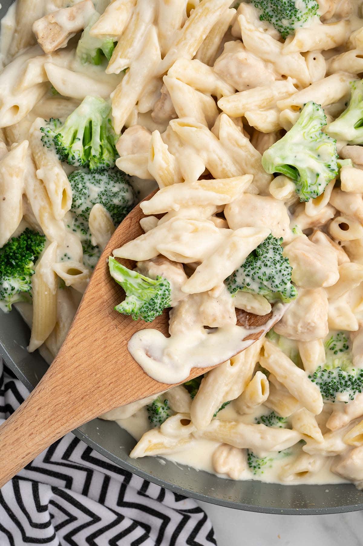 Chicken and Broccoli Penne Alfredo being stirred with a wooden spoon.