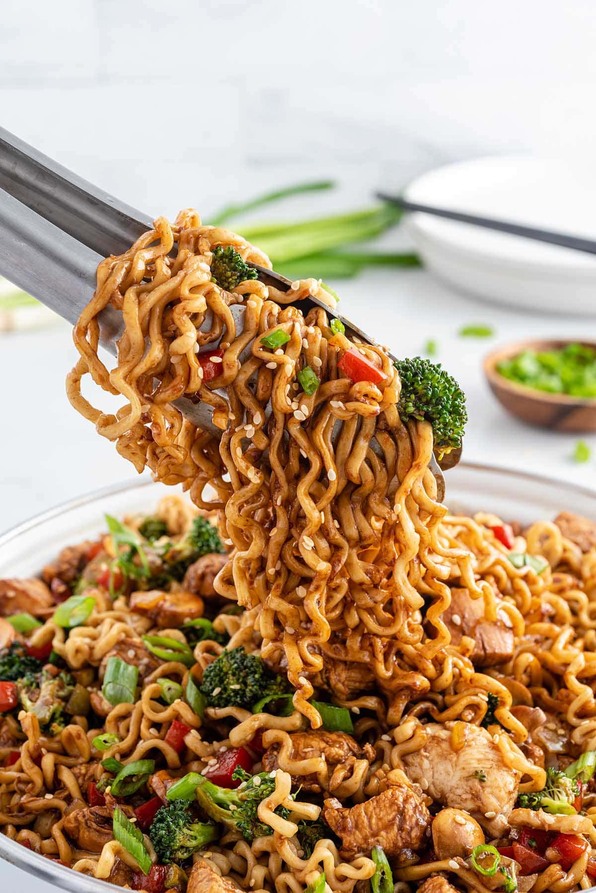 taking Chicken Ramen Stir Fry from a bowl using a tong. 